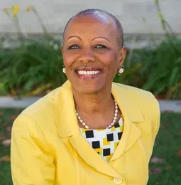 A woman in a yellow jacket is smiling for the camera.