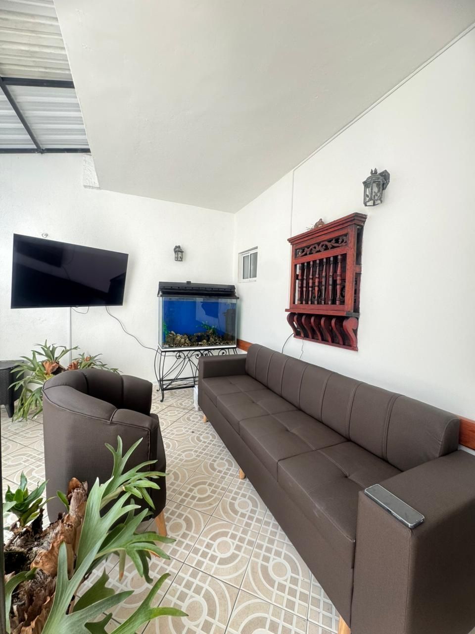 Patio moderno con sofás marrones, suelo de baldosas estampadas, televisor montado en la pared, pecera y estante de pared rojo.