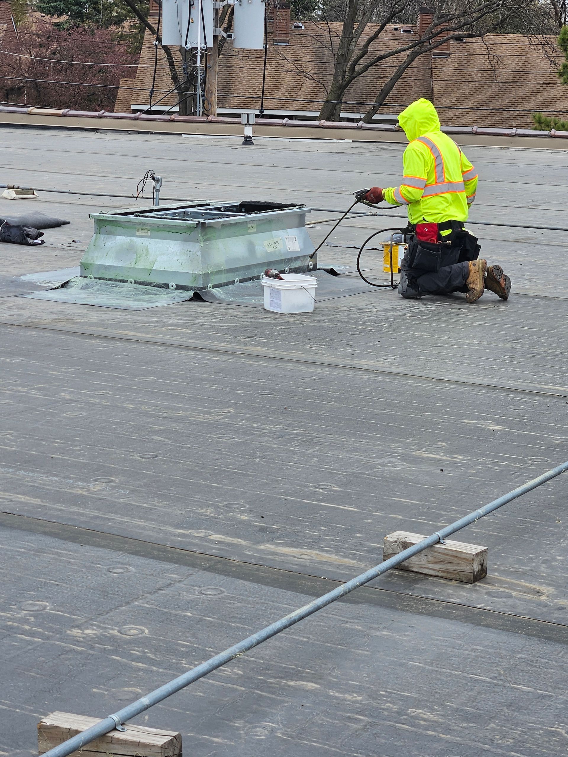Worker in neon safety gear kneels on a rooftop beside HVAC equipment and tools.