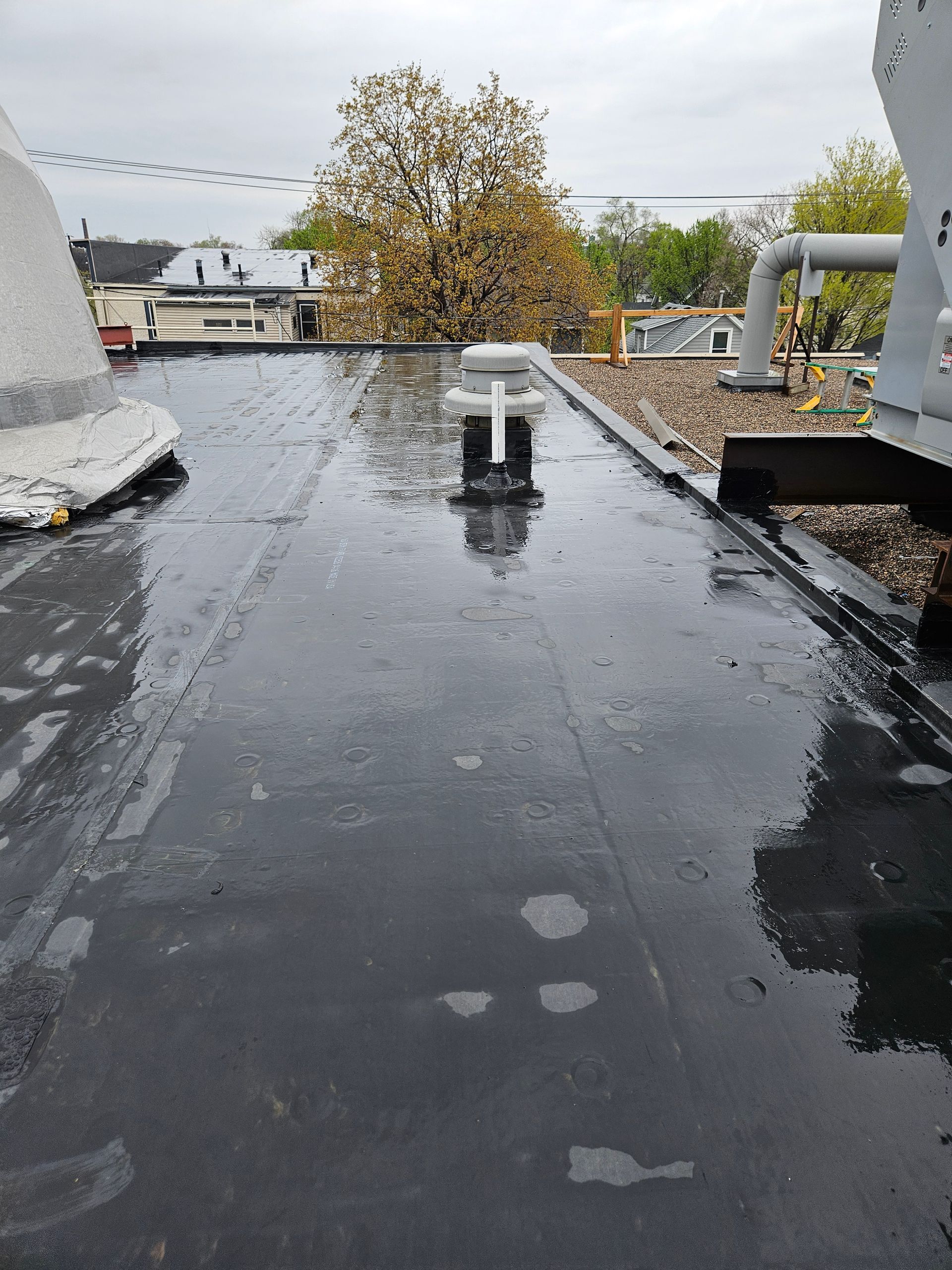 Wet black rooftop with small vents, white pipes, and a cloudy sky in the background