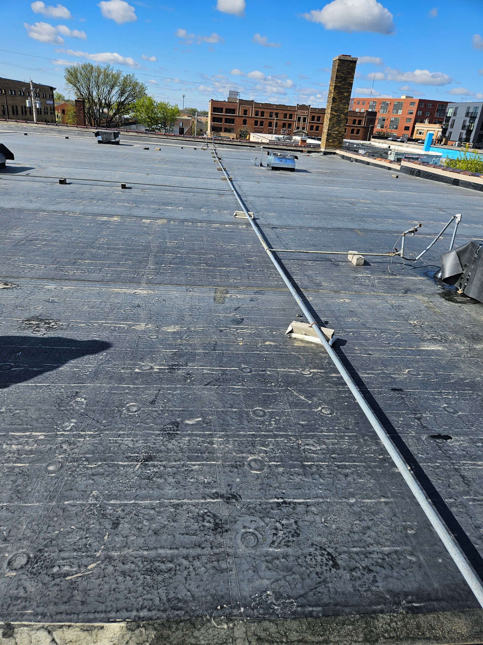 Rooftop covered in black waterproof membrane with scattered debris and a metal pipe under a blue sky