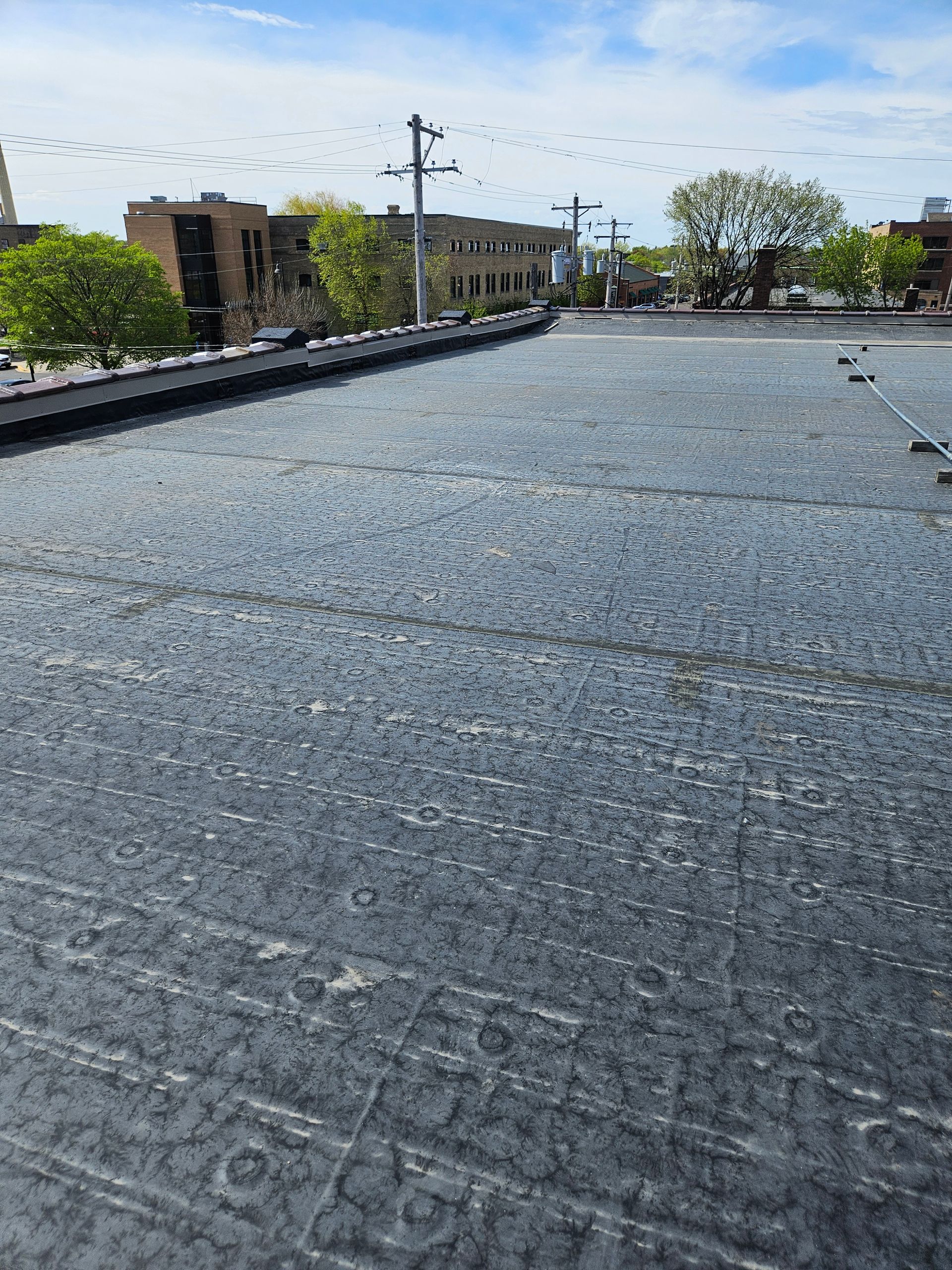 Rooftop with gravel surface, utility poles, and low buildings under a clear blue sky.