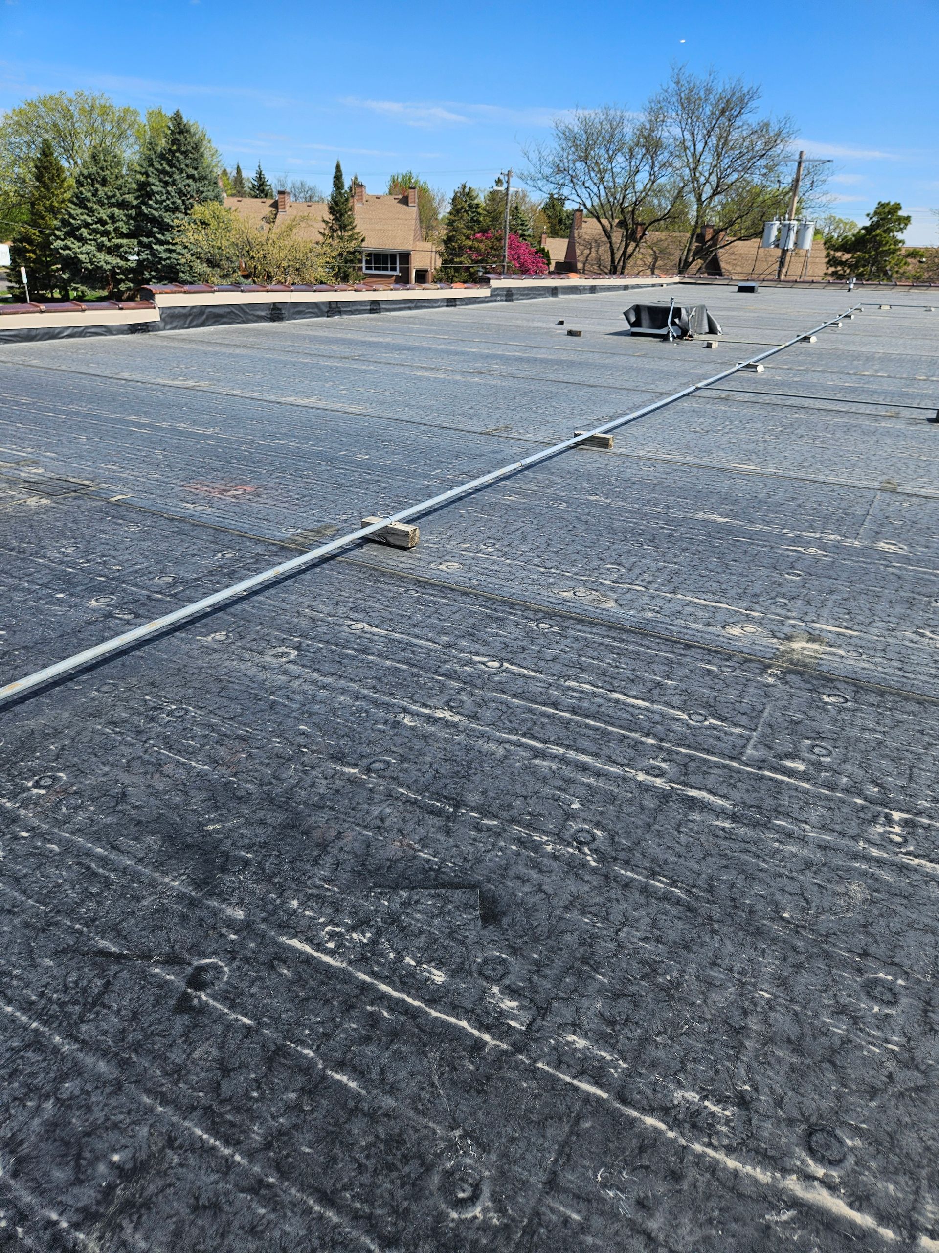Flat rooftop with gray gravel surface, vents, and tree-lined buildings under a clear blue sky