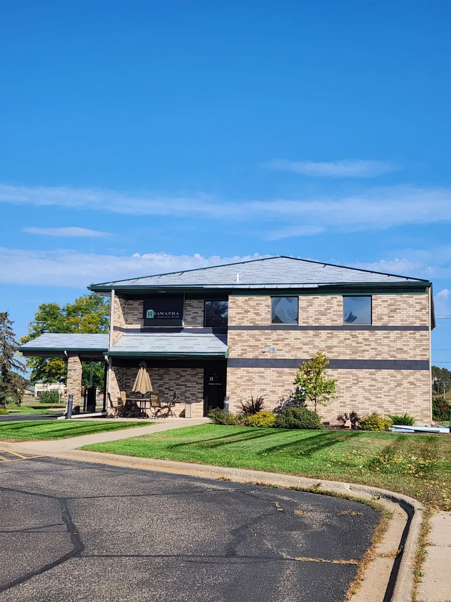 Two-story brick house with blue roof, front porch, and driveway under a clear blue sky