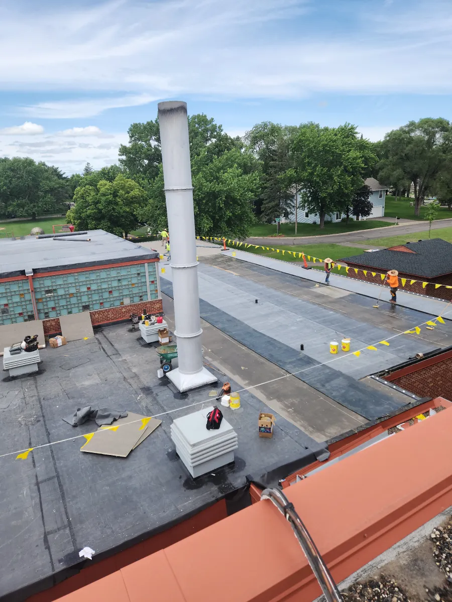 Rooftop with a tall white chimney, utility units, and orange safety barriers under a cloudy sky