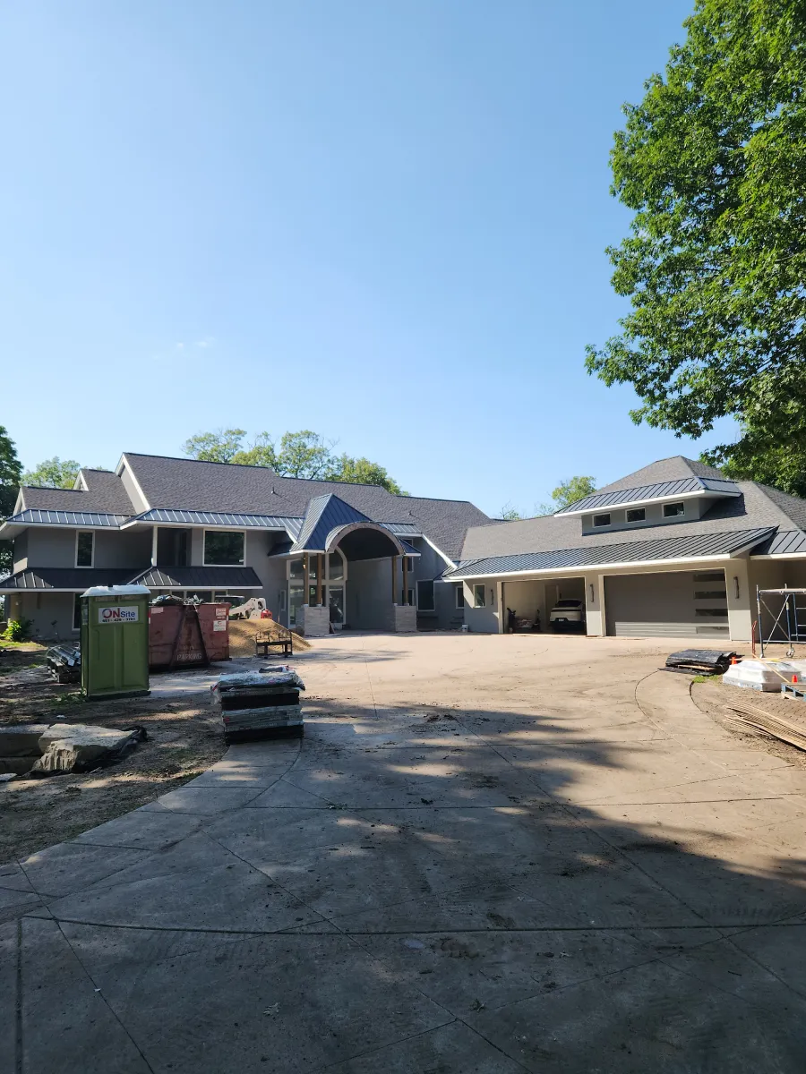 Wide driveway with a large house and outbuildings under a clear blue sky, trees in the background