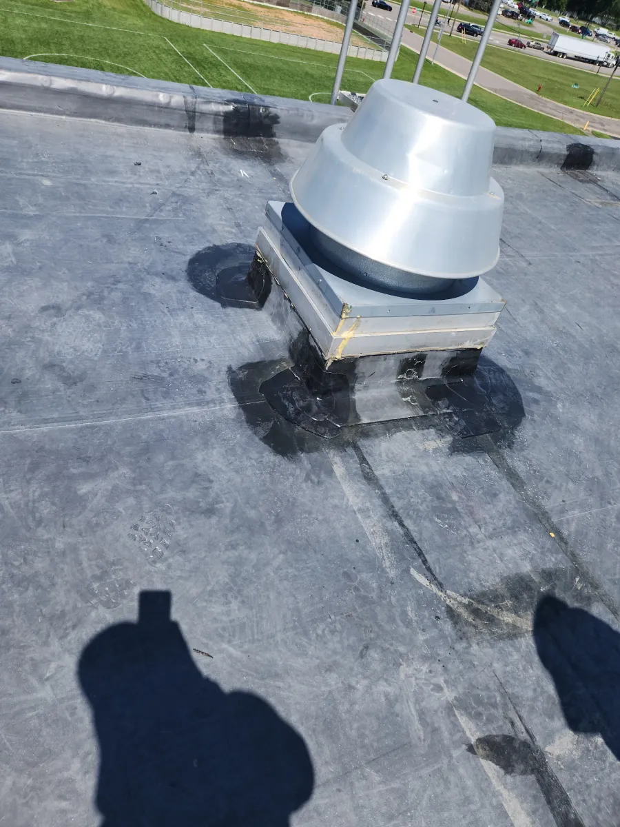 Rooftop HVAC vent unit on a flat black roof near a grassy area