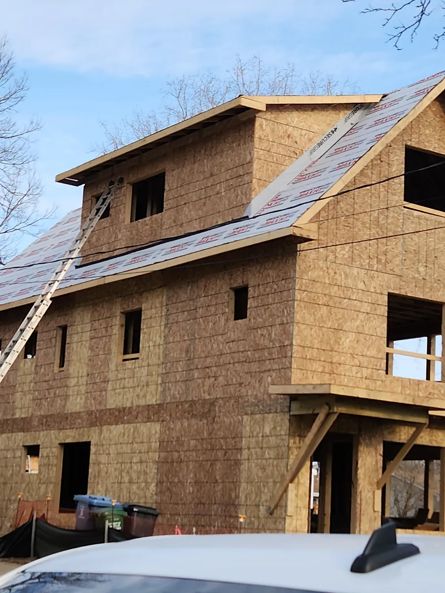 Unfinished two-story house under construction with plywood sheathing and roof underlayment.