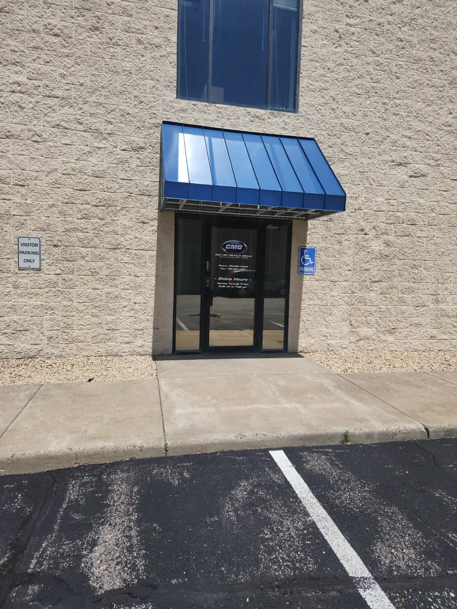 Building entrance with blue awning and glass door in a beige brick wall, next to a parking lot