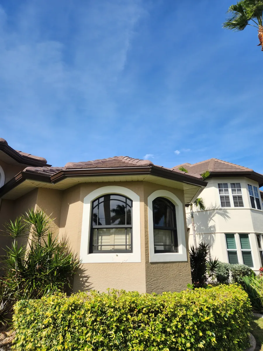 Suburban house with arched windows, beige stucco walls, tiled roof, and green hedges under a blue sky