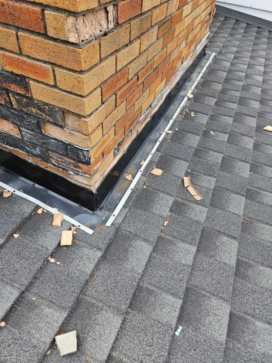 Brick chimney base on a shingled roof with scattered debris nearby