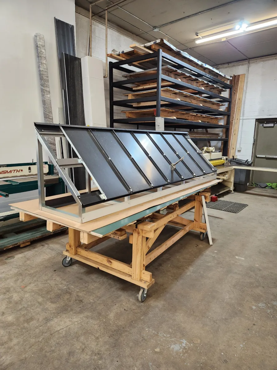 Tilted black metal panel on a wooden stand in an industrial workshop, with shelving in the background