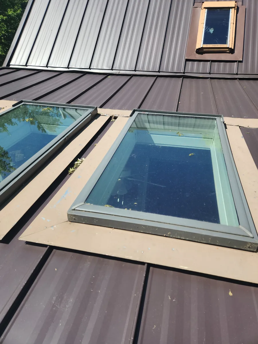 Rooftop with skylights and metal panels, including a beige-framed skylight and a small dormer window.