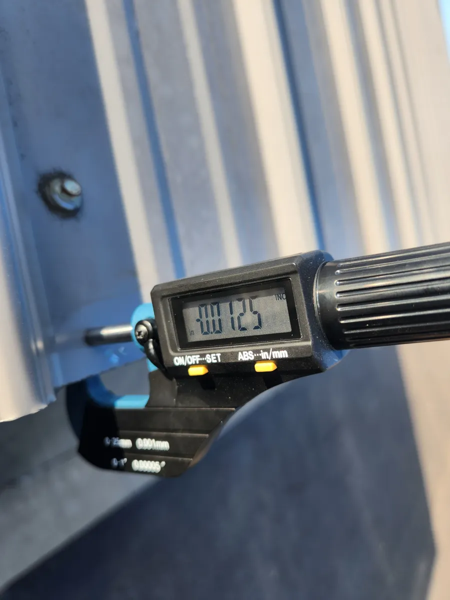 Digital caliper measuring a metal bolt on a gray panel, close-up