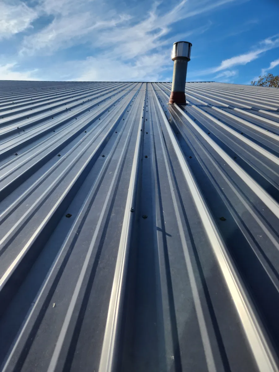 Corrugated metal roof with a rooftop vent under a blue, partly cloudy sky