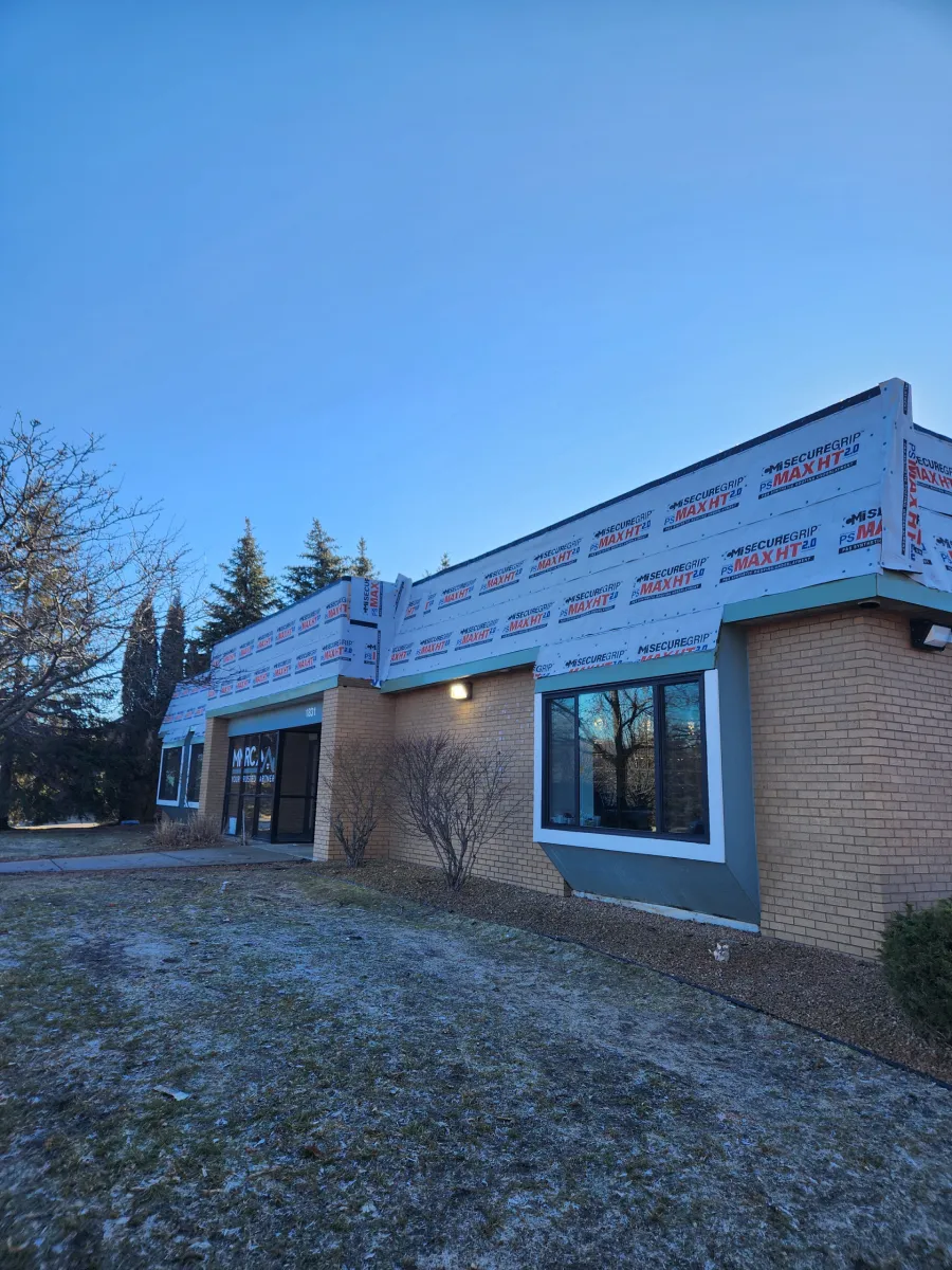Single-story brick house under construction, with exposed roof framing, windows, and a frosty yard at dusk