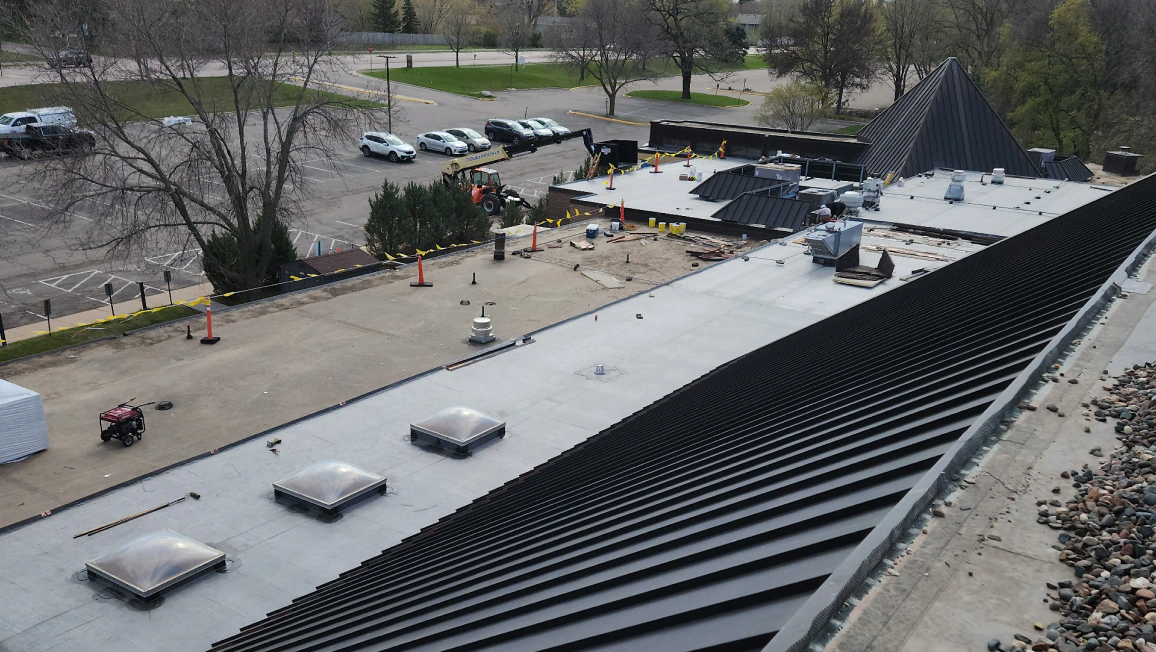 Roof with snow, overlooking a courtyard with trees, parked cars, and a playground area.