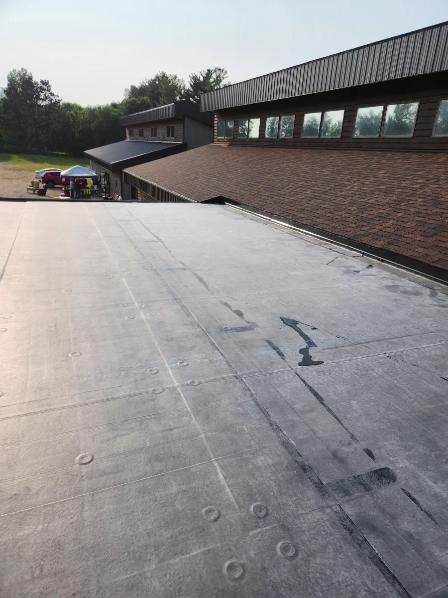 Rooftop with solar panels beside a brick building and trees in the background.