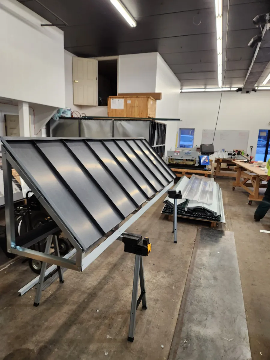 Workshop with a large black metal panel on stands, tools and equipment in the background.