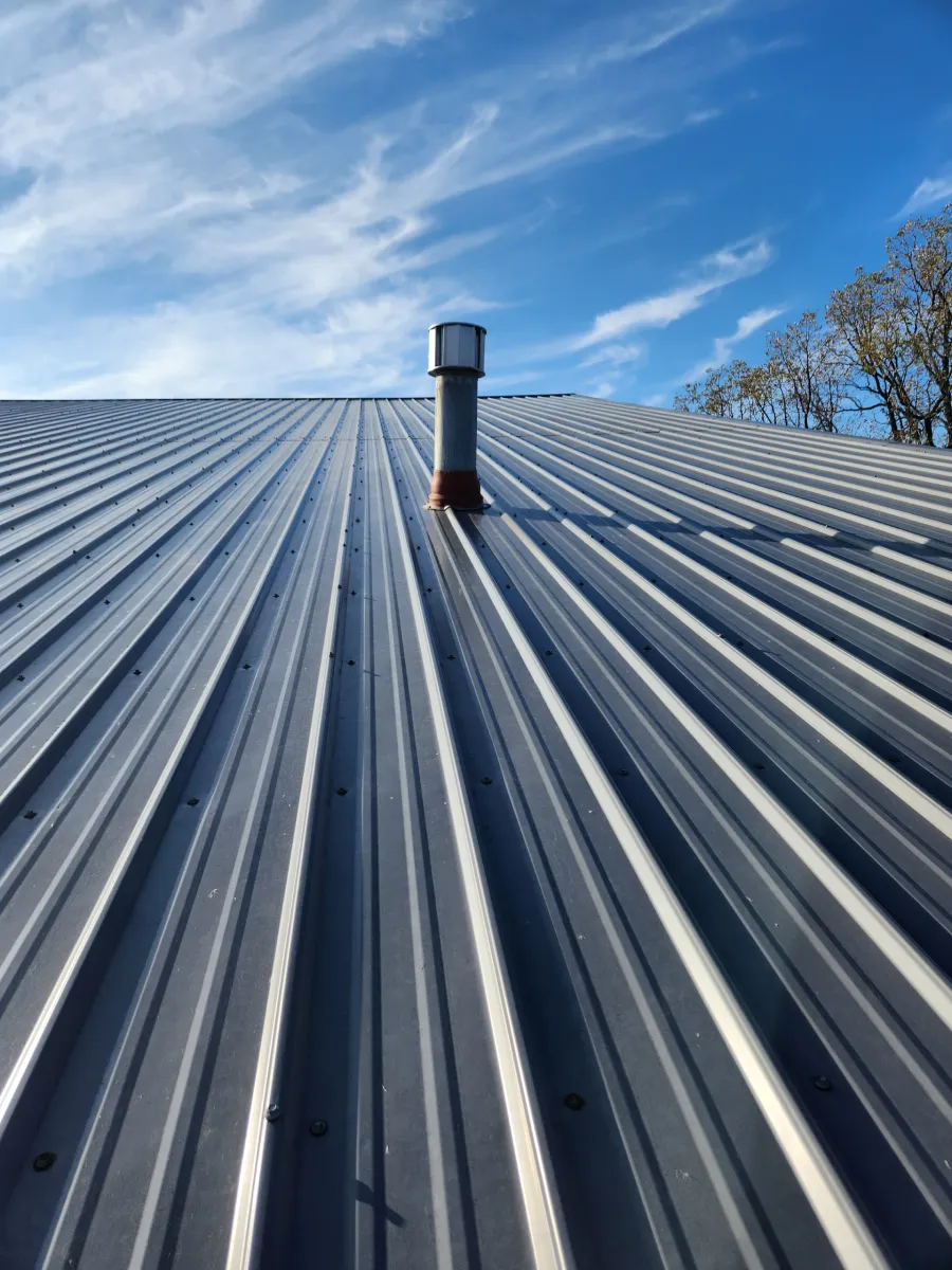 Corrugated metal roof with a central vent pipe under a blue sky
