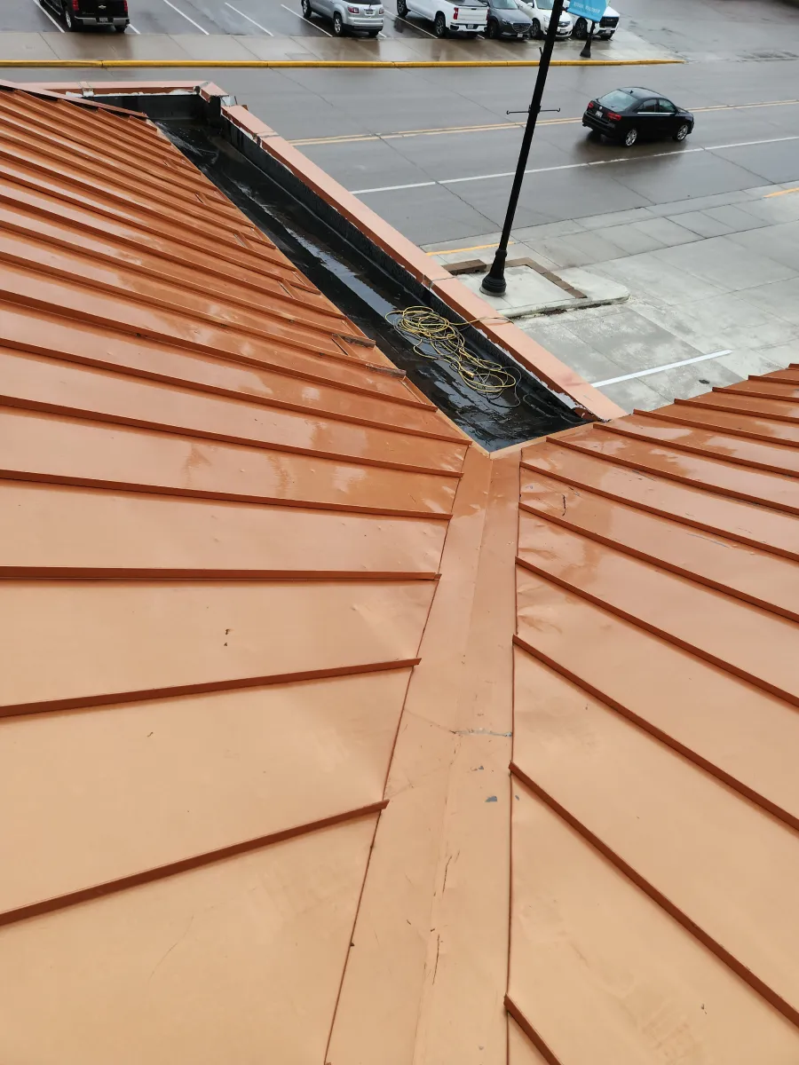 Rust-colored metal roof corner overlooking a wet street with a few cars below