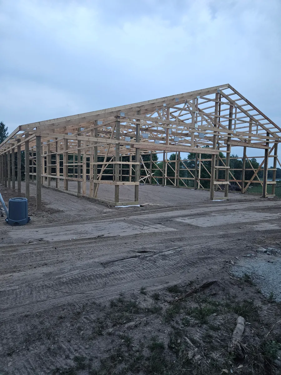 Partially built wooden barn frame on muddy ground at dusk