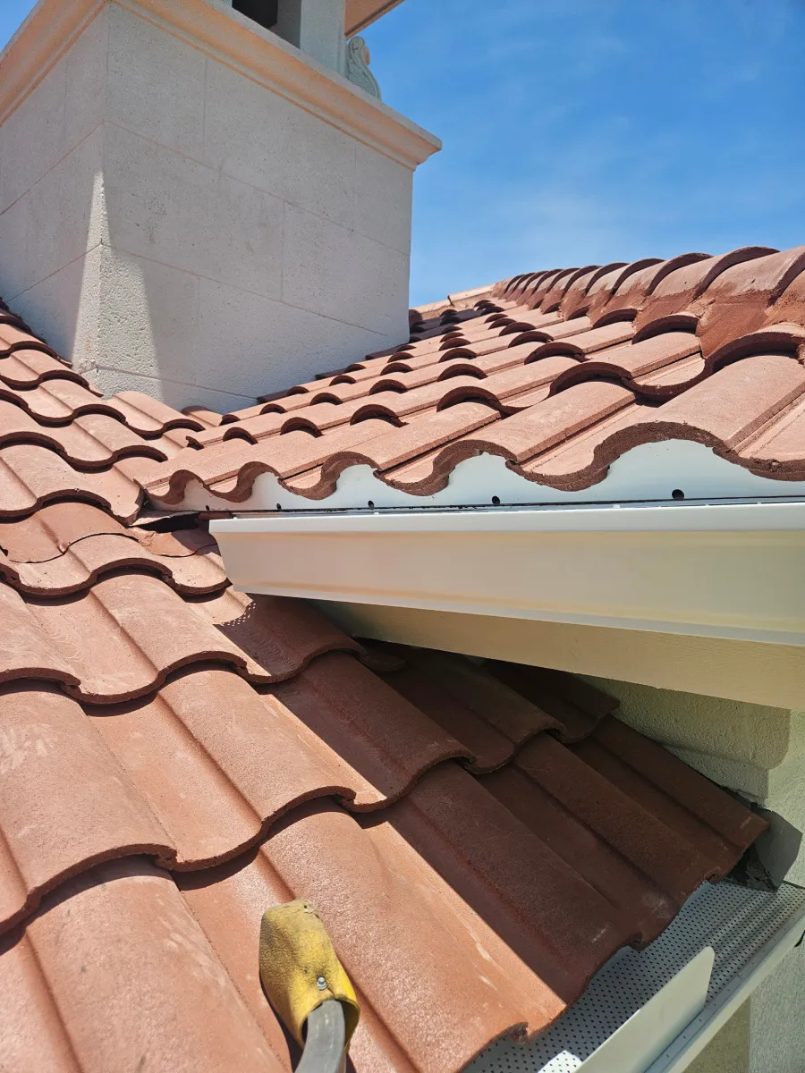 Close-up of terracotta roof tiles with a white chimney and roof edge under blue sky