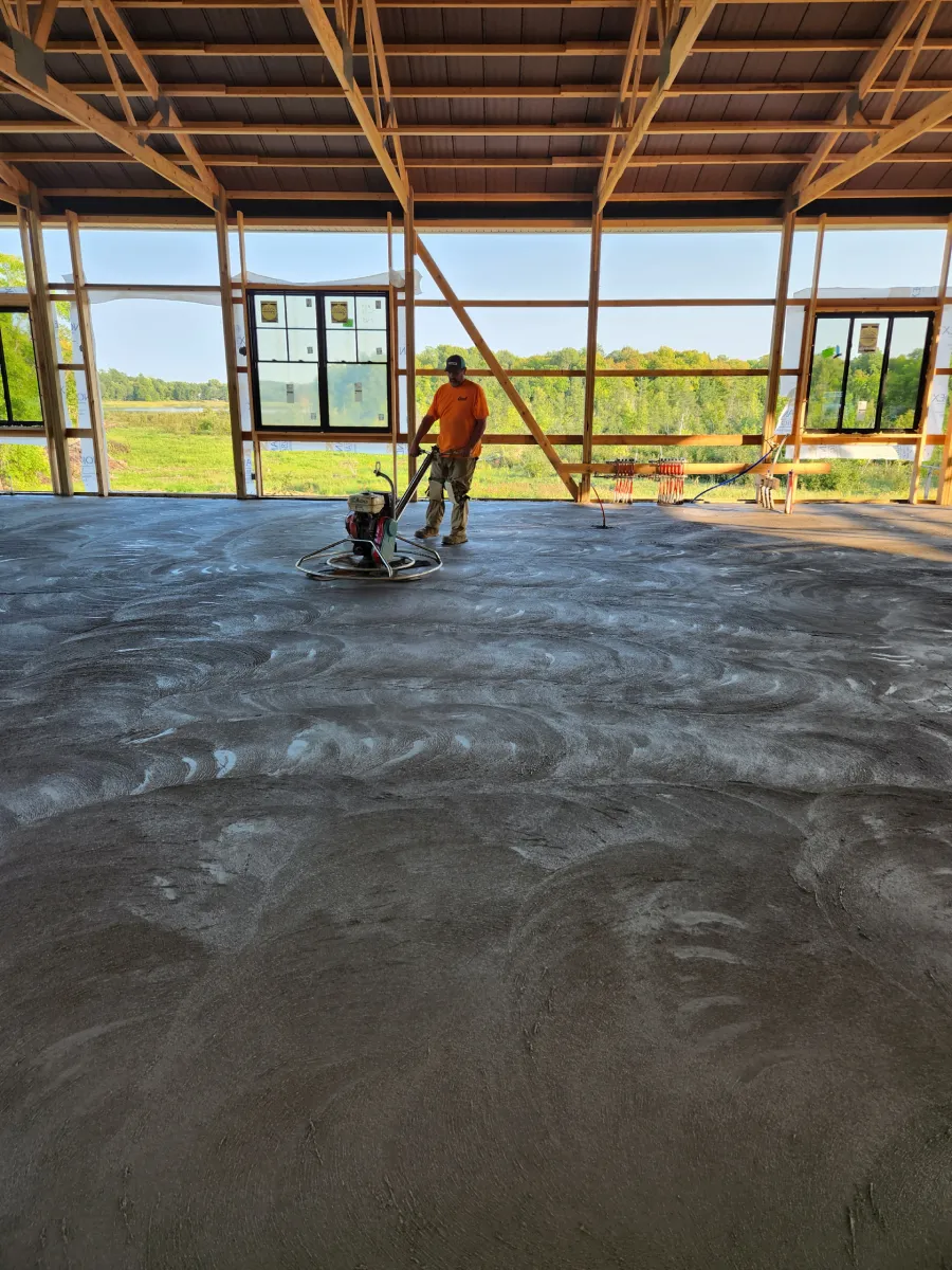 Worker smoothing a wet concrete floor inside a large open building
