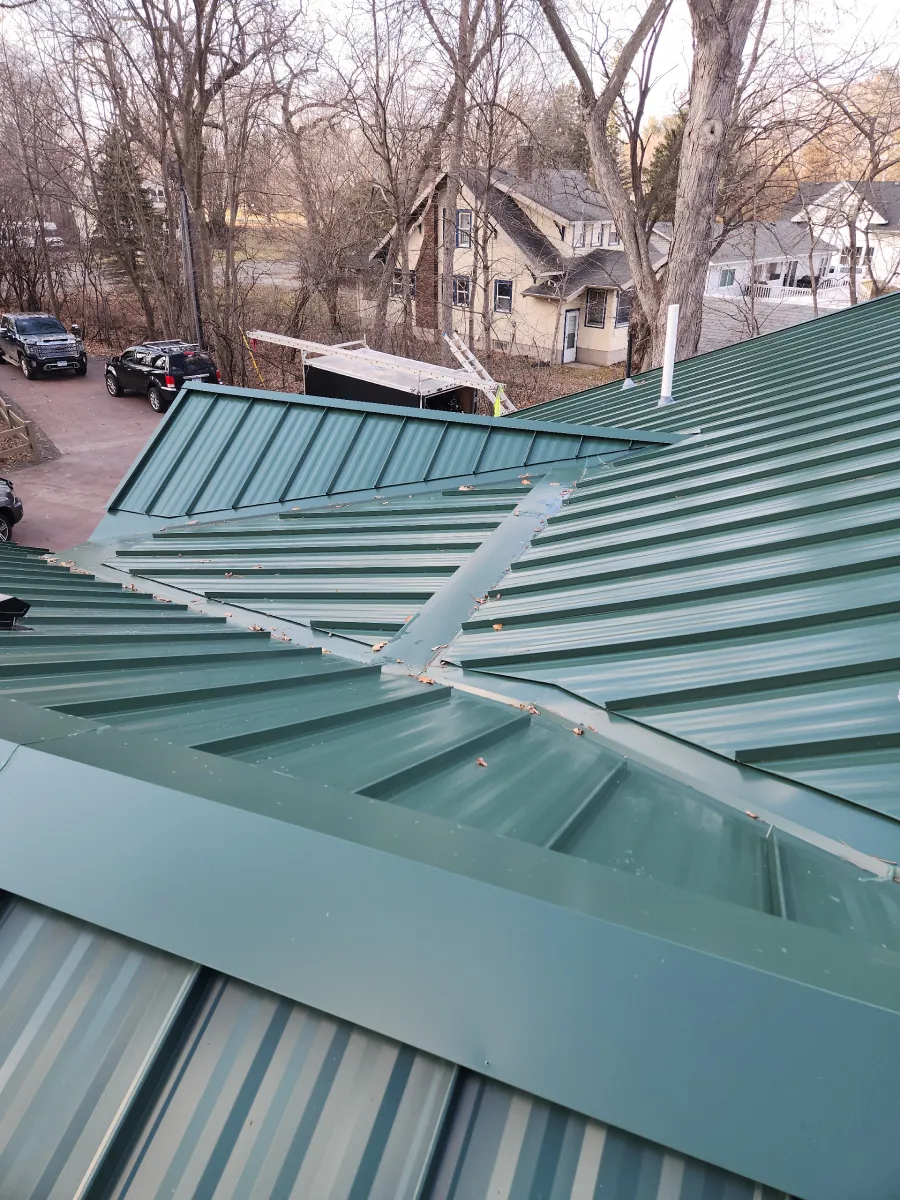 Green metal rooftop with a damaged raised panel overlooking a residential street