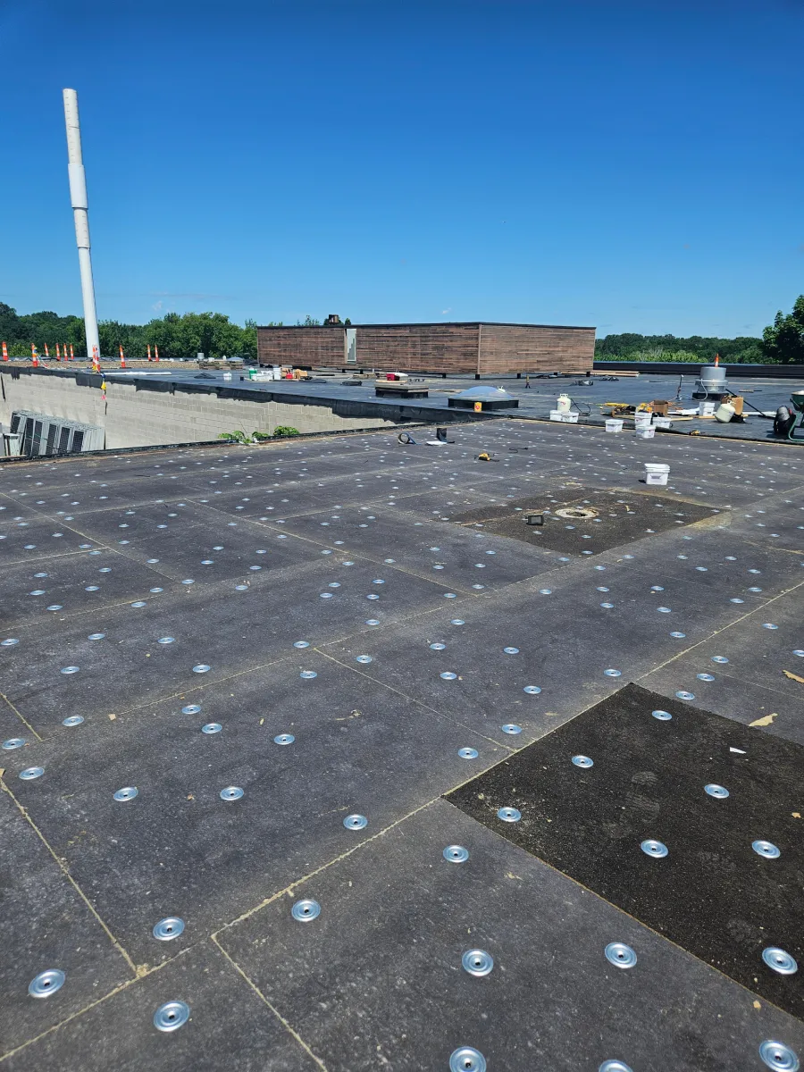 Flat rooftop with gravel and vents under a clear blue sky, with industrial buildings in the distance.