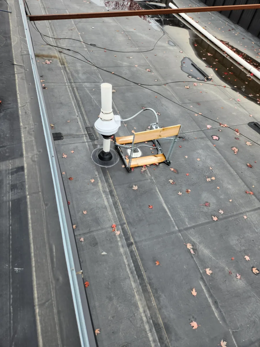 Rooftop with a white vent pipe and yellow equipment on a dark flat roof.