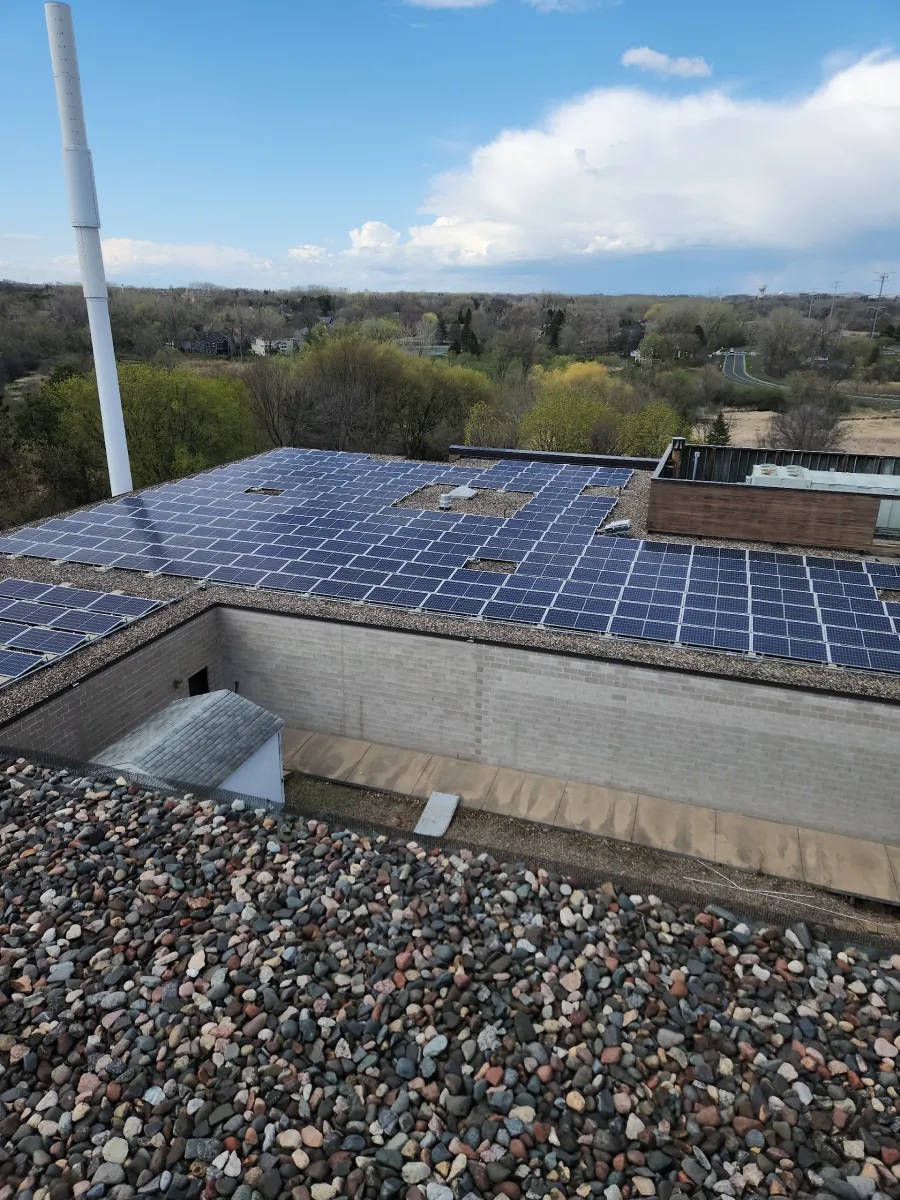 Rooftop with blue solar panels overlooking trees and a cloudy sky