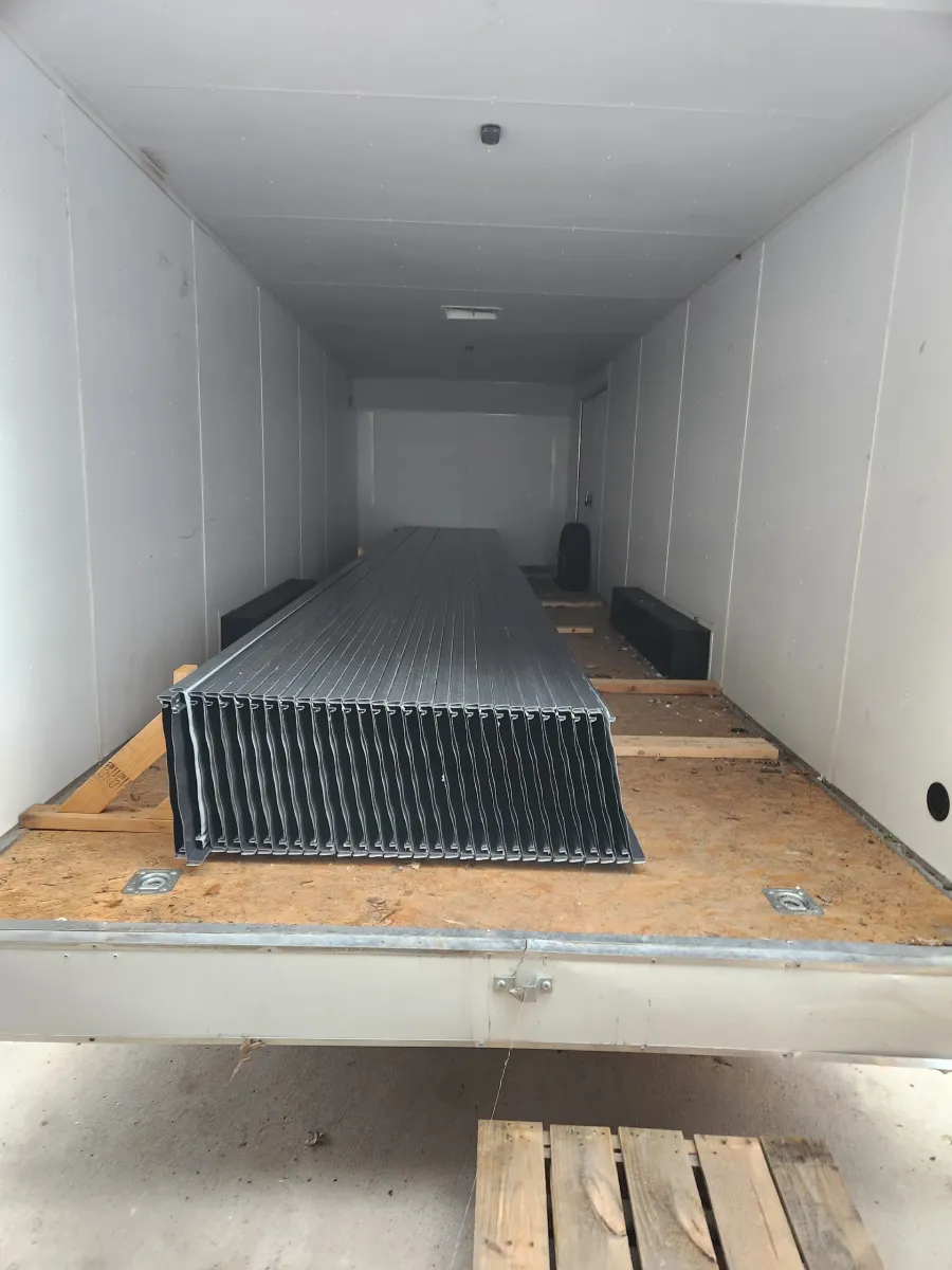 Stacked black corrugated panels on a wooden pallet inside a white truck trailer.