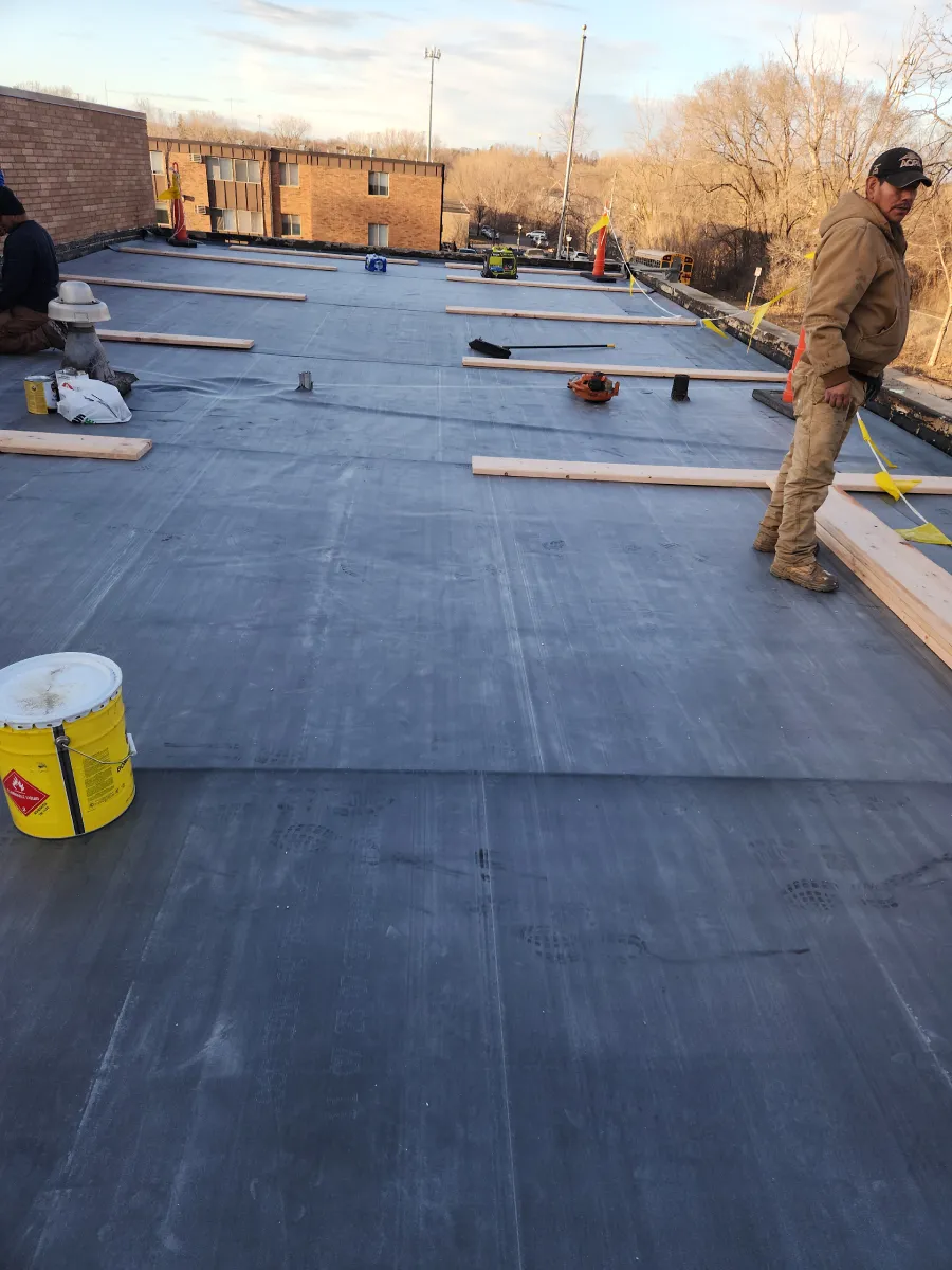Workers installing black roofing membrane on a flat rooftop at sunset