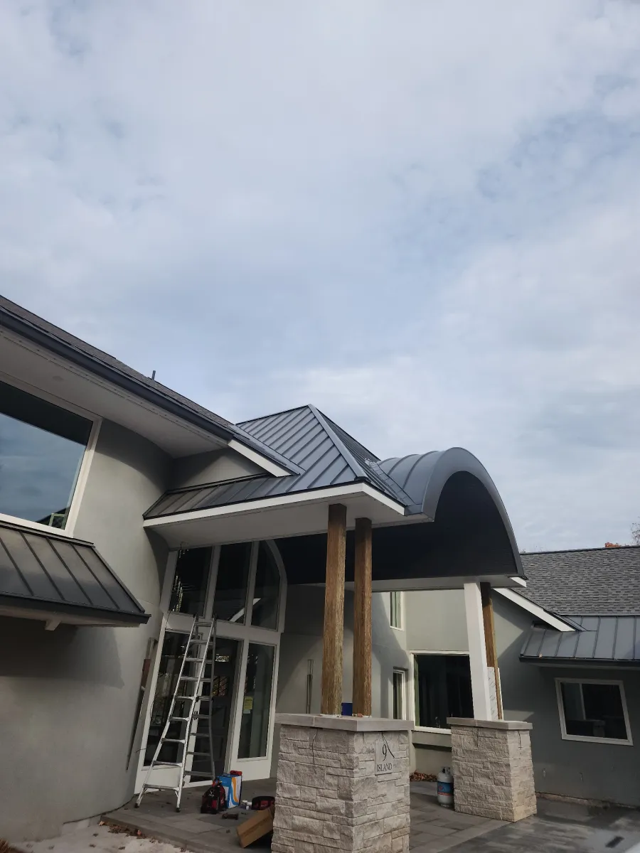 House entrance under construction with scaffolding, ladder, and unfinished roof shingles.