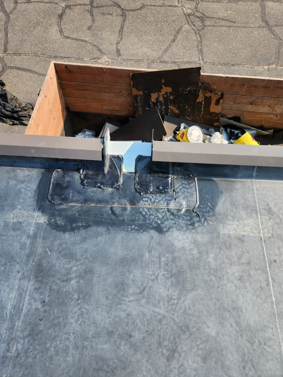 Damaged roof vent opening with exposed wood and debris on a flat rooftop