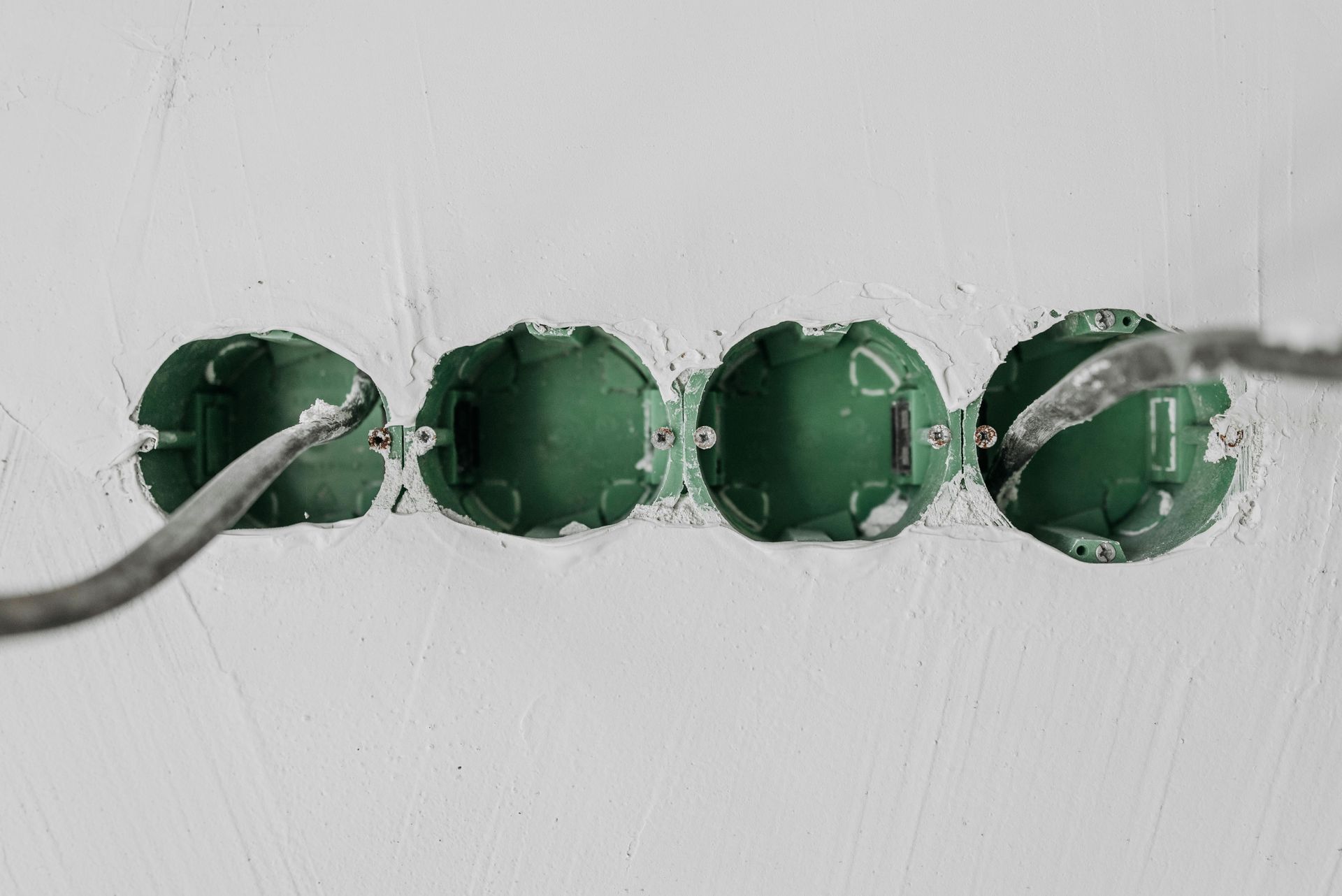 Green electrical boxes in a white wall, wires inserted, ready for installation.