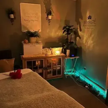 Cozy massage room with warm lighting, plants, wall decor, and teal LED lights along the floor.