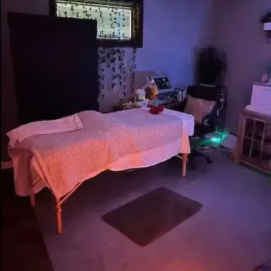 Dim therapy room with massage table, black cabinet, chair, and purple ambient lighting.