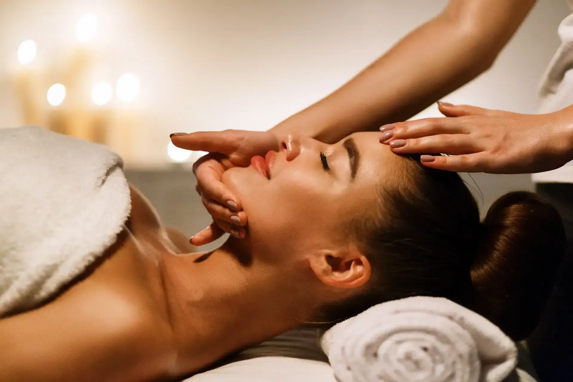 Spa massage with a client lying on a table while a therapist gently massages the face and forehead.
