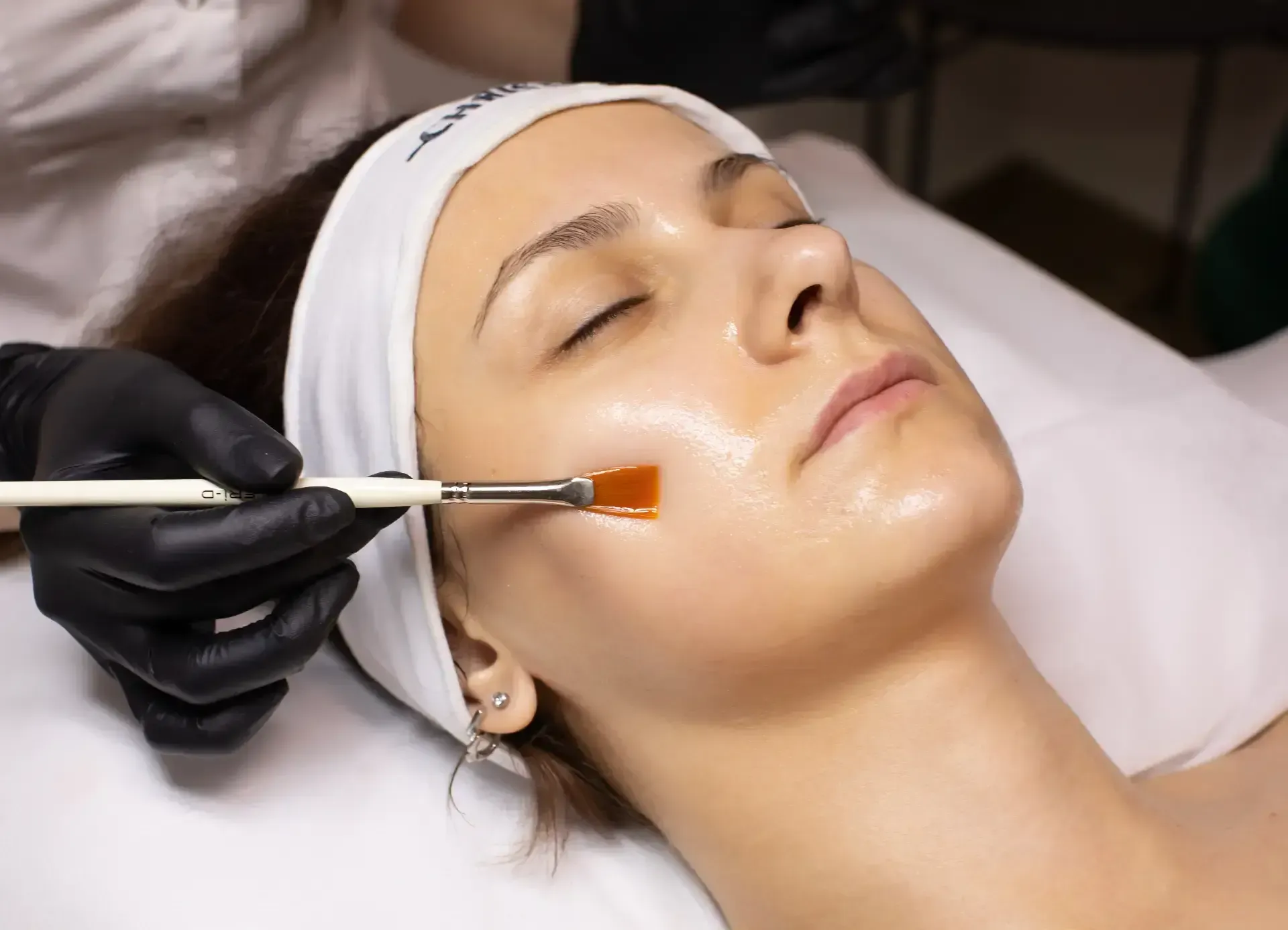 Facial mask being applied with a brush to a reclining client in a spa treatment