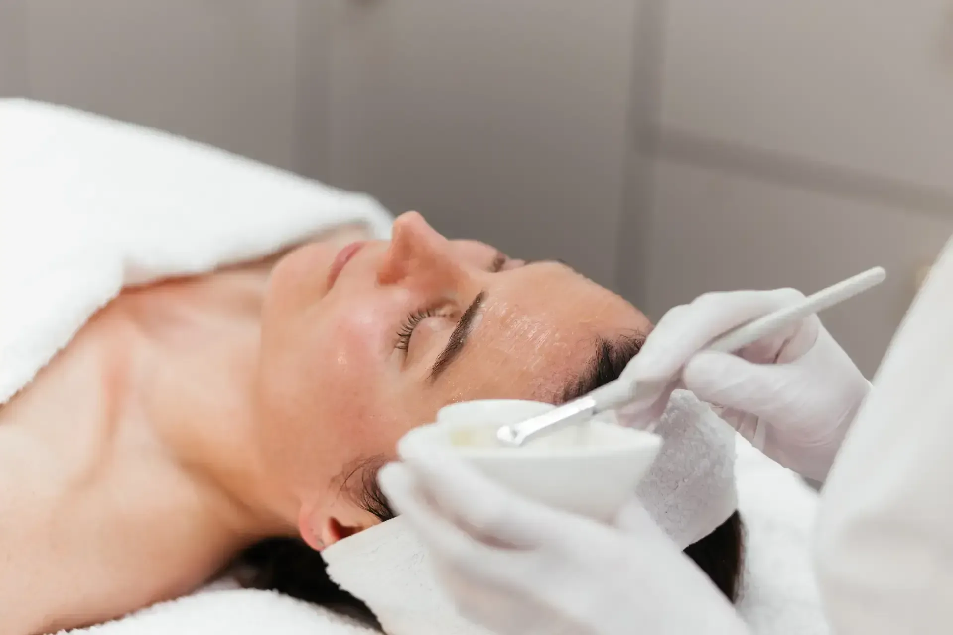 Spa skincare products with rolled white towels and green leaves on a warm beige background