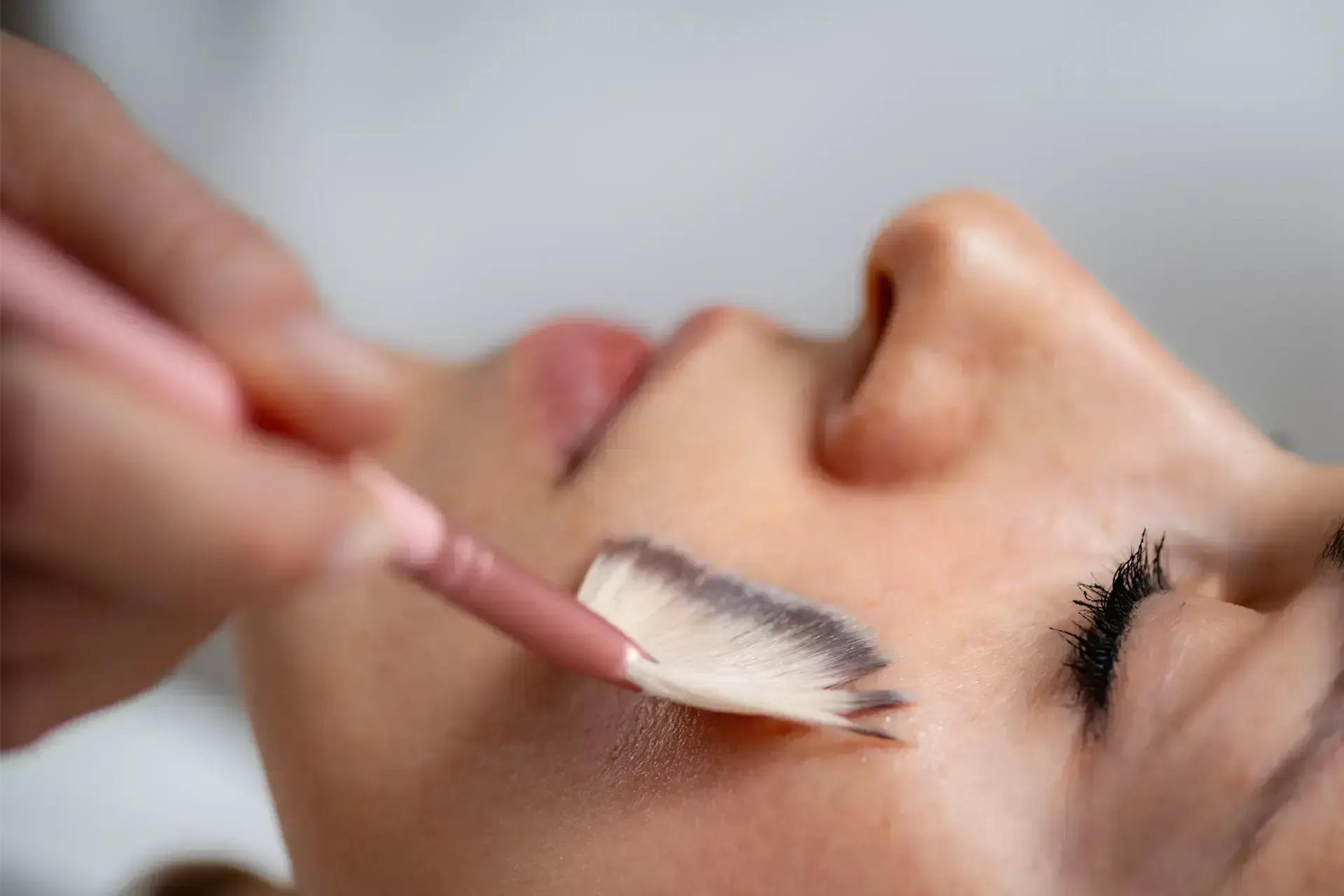 Makeup brush applying eyeshadow to a closed eye on a person's face