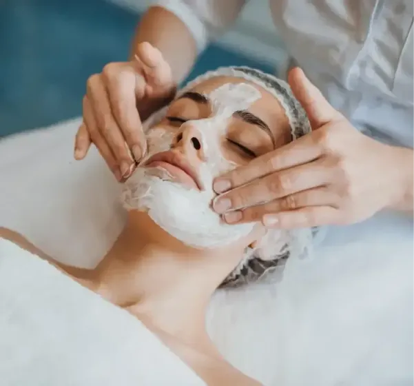 Facial treatment with white mask applied as hands massage a woman’s face on a spa bed
