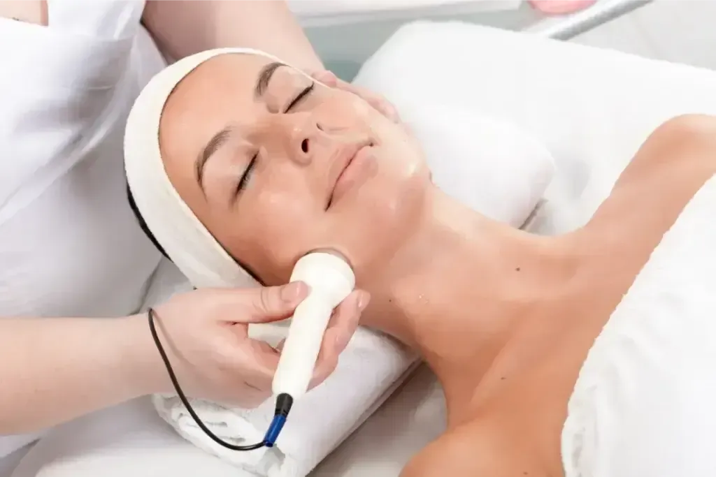 Woman receiving a facial treatment with a handheld device while lying on a spa bed
