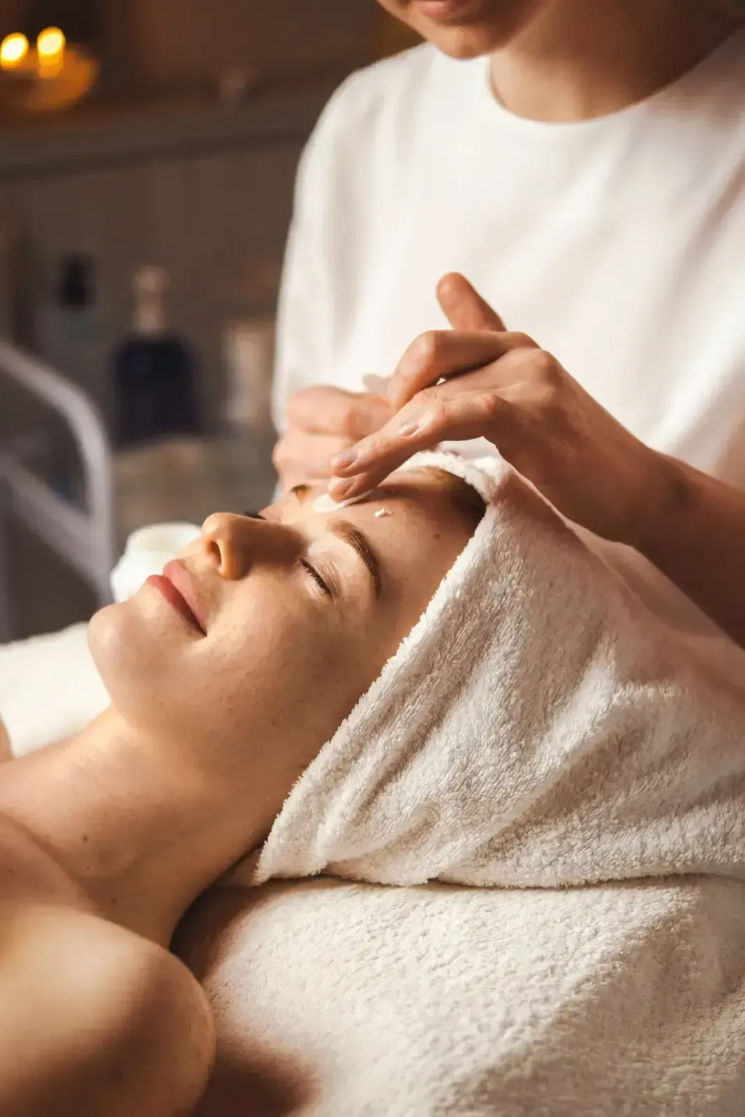 Spa therapist applying facial treatment to a client with a towel wrapped around her head