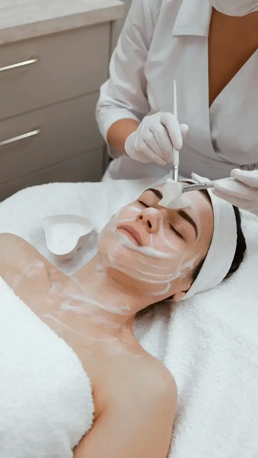 Facial treatment in a spa, with a woman lying down as a clinician applies serum to her face