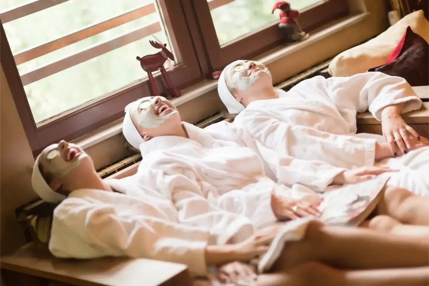 People reclining on massage beds in white robes with face masks in a spa room