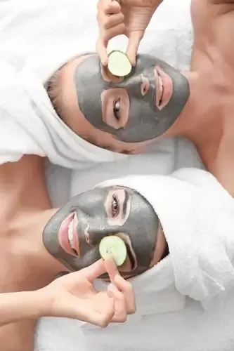 Two people lying down with gray facial masks, each applying cucumber slices to their eyes.