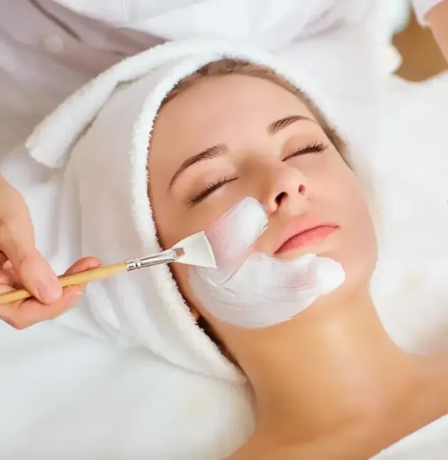 Woman receiving a white facial cream treatment with a brush while lying on a spa bed